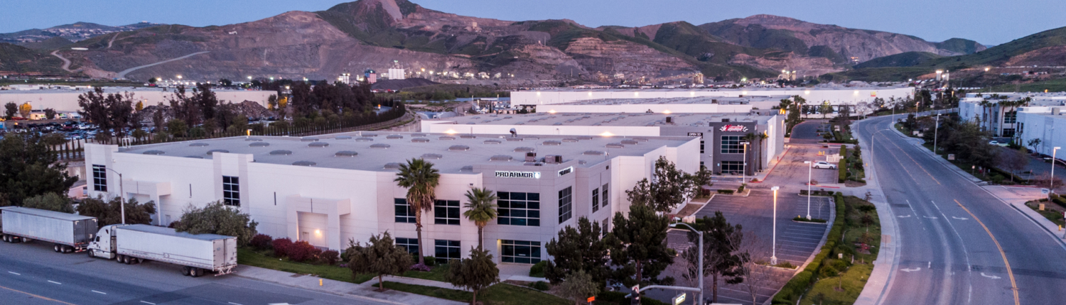 A photo taken at twighlight of a large industrial building with Proarmour sign and mountains in the background