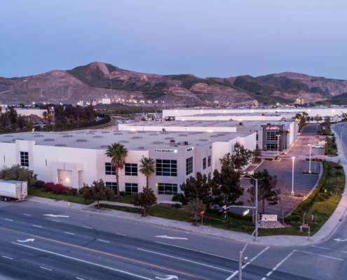 A photo taken at twighlight of a large industrial building with Proarmour sign and mountains in the background