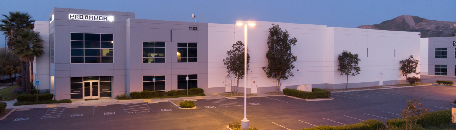 A photo taken at twighlight of a large industrial building with Proarmour sign and mountains in the background